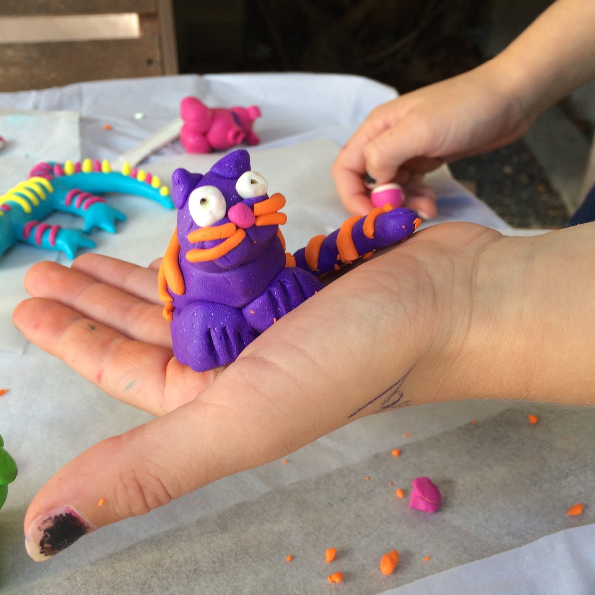 A child holding a purple and orange clay cat at a Klay Master workshop