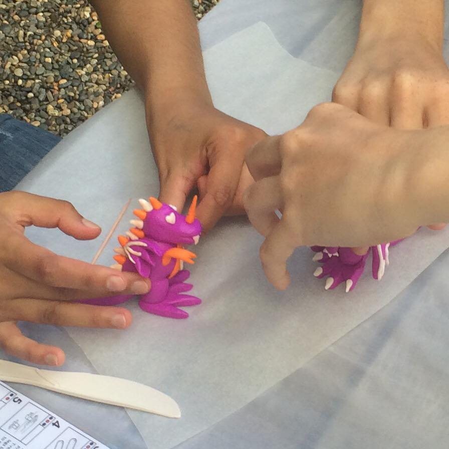 Hands shaping a clay creature on baking paper